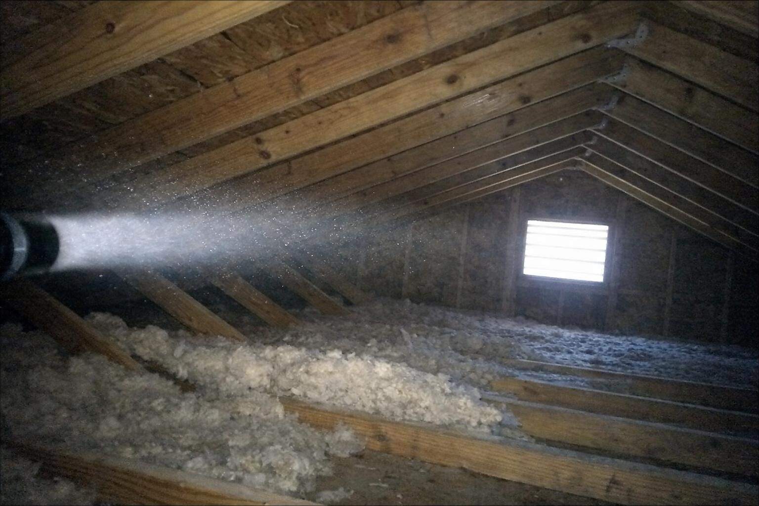A flashlight beam across attic rafters and roof decking