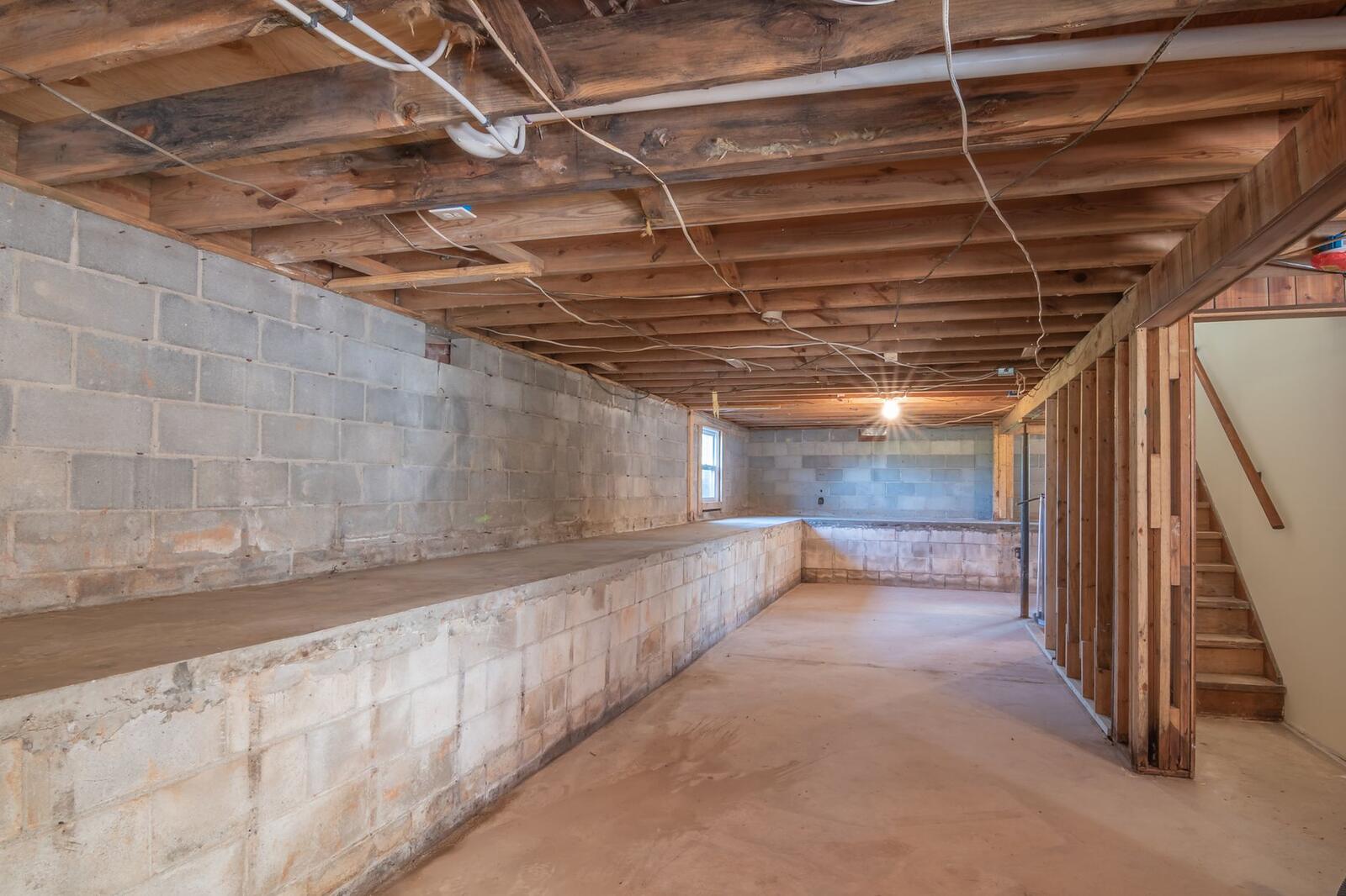 The dark crawl space under a pier-and-beam house with wood floor joists overhead